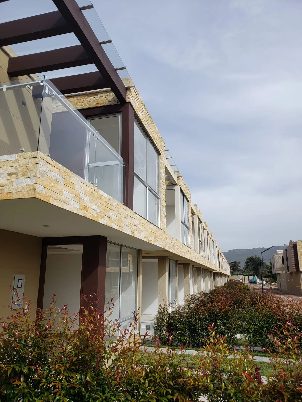 Foto real del corredor lateral de Bosco Reservado con casas terminadas, ventanales grandes y cerros de Chía al fondo