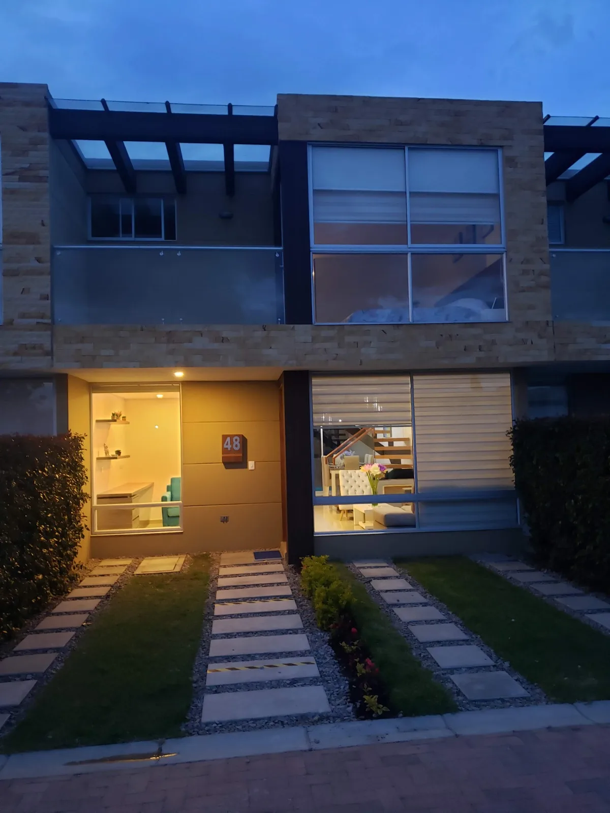 Foto real cinematográfica al atardecer de la casa 48 de Bosco Reservado con luces interiores encendidas y jardín